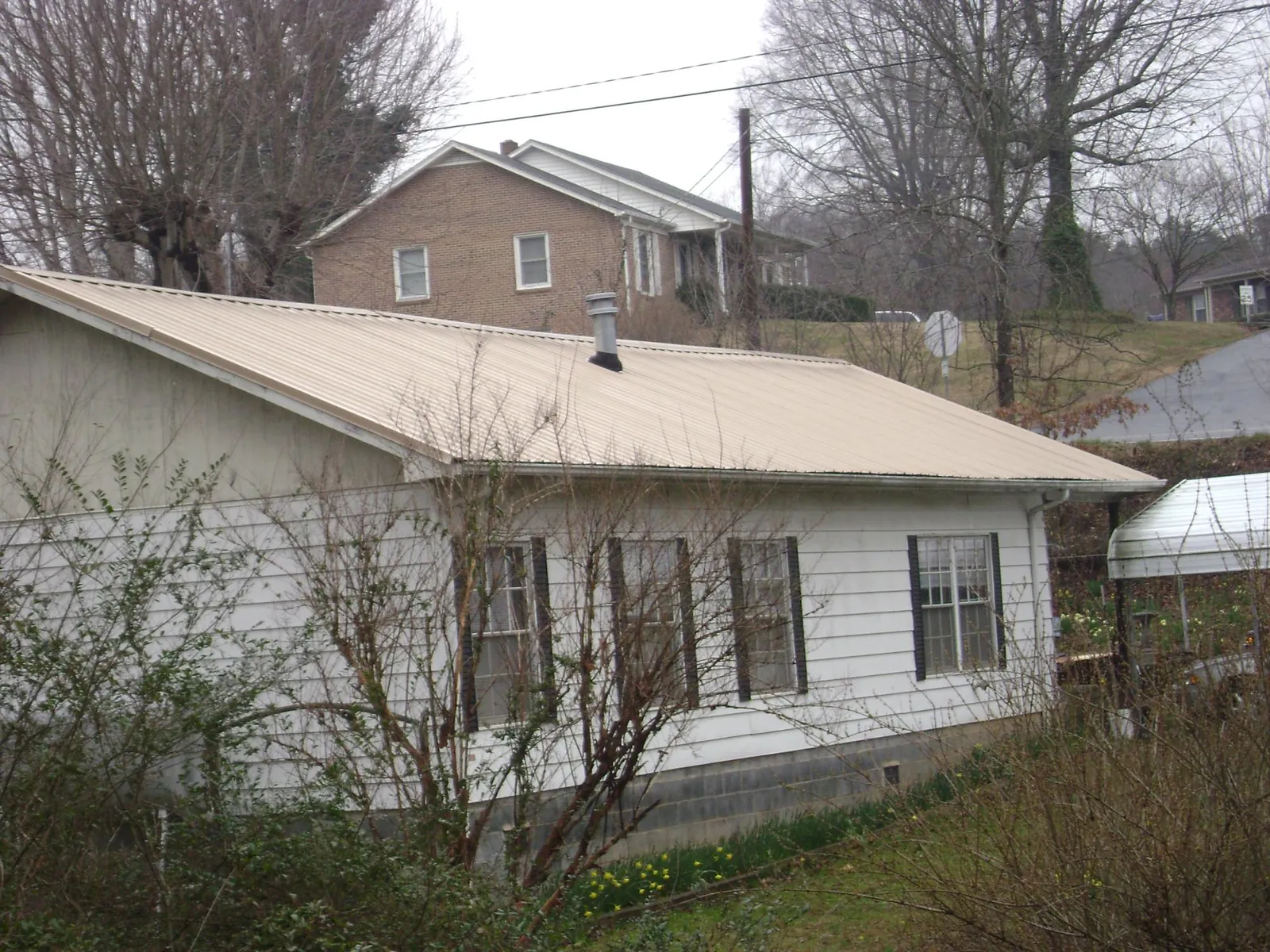 Tan metal roof on a white sided house set into a hillside — Commercial Roofing by Roofing Brothers in Dexter